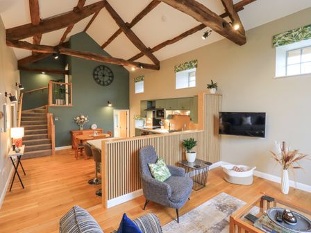 An open living area with wooden beams a staircase dining table kitchen and seating at Old Howgate Barn Outgate near Hawkshead