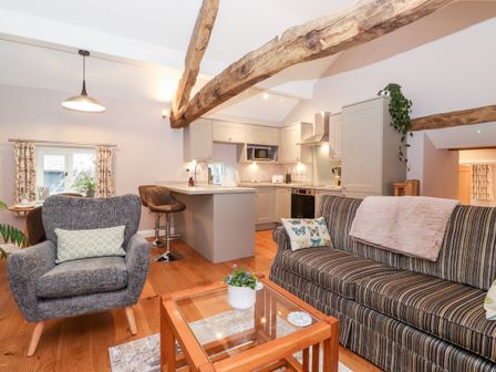An open plan living room and kitchen with wooden beams a striped sofa a grey armchair a glass coffee table and bar stools at Low Ashmead Cottage in Hawkshead