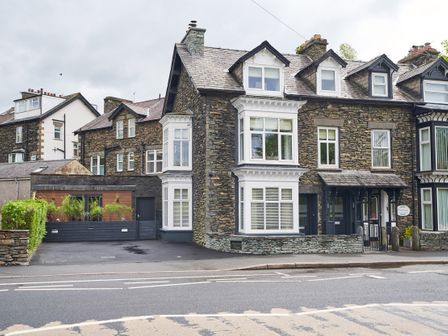 A stone house with white framed windows and a black door next to a small driveway at Upper Sheriff's Place in Windermere