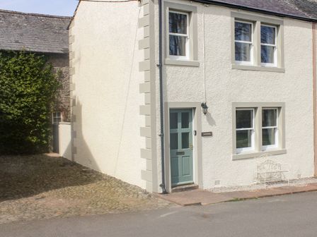 Exterior of a white house with four windows a green door a bench and cobblestone driveway at Rayside Ullswater