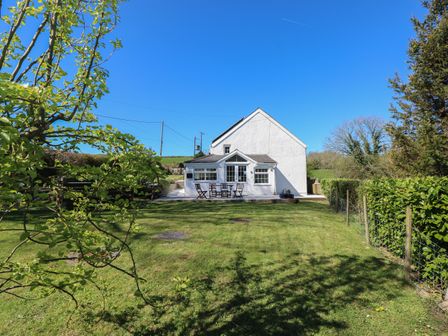 A white house with a patio and outdoor furniture in a garden with grass and trees at Little Bobbins in Saundersfoot