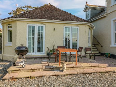 An outdoor patio with a round grill a wooden table and four chairs outside a house at The Hideaway in Thurlestone