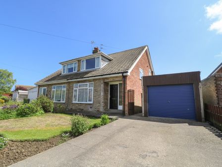 A semi detached house with a garden and a garage with a blue door at 4 Ranby Drive in Hornsea