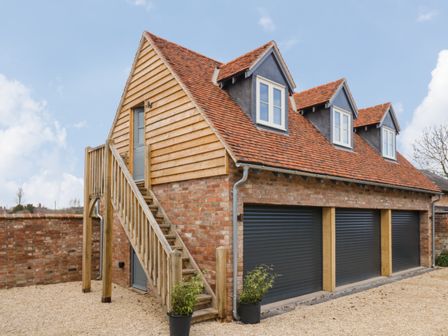 A brick garage with three black roller doors wooden stairs leading to an upper floor with three dormer windows at Coach House Mews in Alderminster