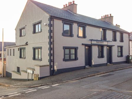 A grey building with multiple windows and two doors marked the bull on a street corner at The Bull Inn in Deiniolen