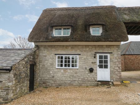 Stone cottage with thatched roof and white door with windows at Laurel Cottage in Osmington