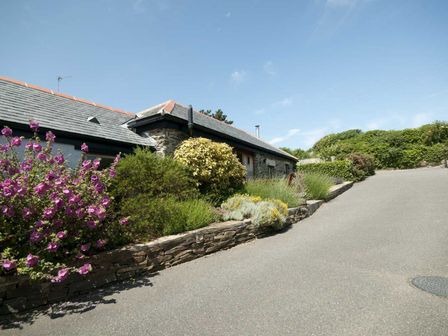 A stone building with a sloped roof next to a garden with flowers and bushes at Lavender Barn in Crantock