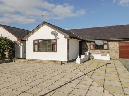 A paved driveway and front yard with a white building and a garage at Rhos Deiniol in Morfa Bychan