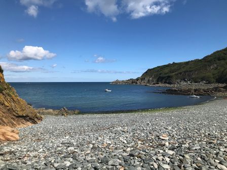 A rocky beach with two small boats on water and hills in the background at The Old Stable in Porthallow