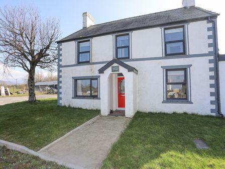 The exterior of a two-story white house with gray trim and a red door with a walkway and grass at Bryn Afon Farm in Llanrug