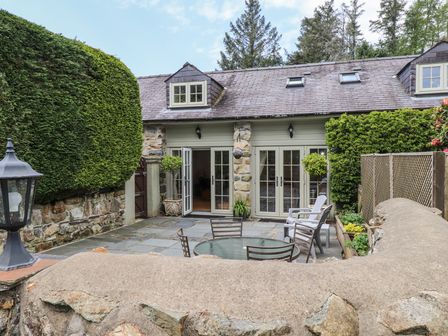 A stone patio with outdoor table and chairs outside a stone and wood house at Garden Cottage Garndolbenmaen near Tremadog