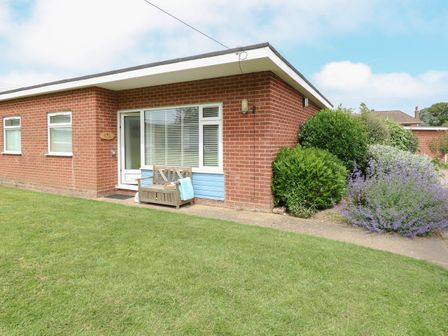 A brick house with a bench and plants outside on a lawn at The Nook in Mundesley