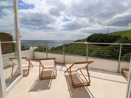 A balcony with three wooden deck chairs overlooking the ocean and green hills at Ocean View in Downderry