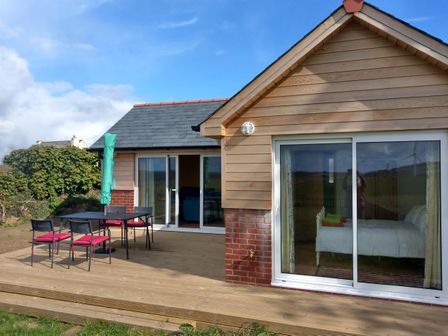 A wooden deck with a table and four chairs outside a house with sliding glass doors at Orchard Chalet in Horningtops near Liskeard