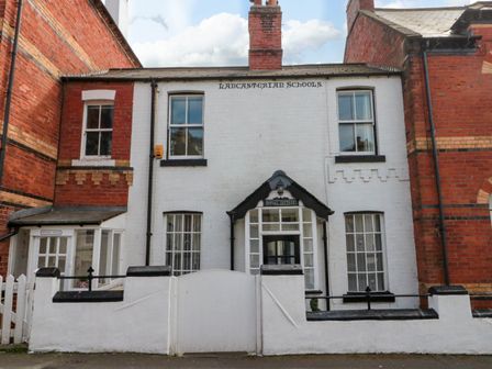 A white cottage with black trim between two red brick buildings with a white wooden gate and signs reading lancasterian schools rydal cottage and school house at Rydal Cottage in Scarborough