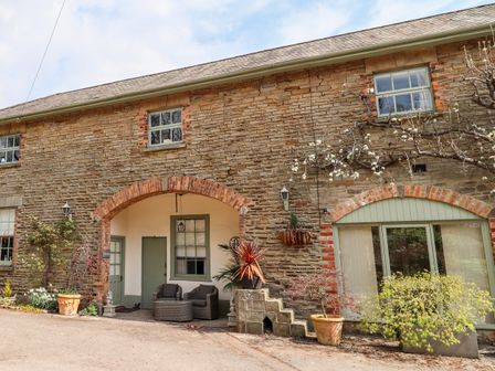 A stone house exterior with green framed windows and doors and plants at The Stable in Lydney