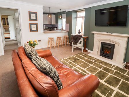 A living room with a leather sofa cushions a fireplace wall-mounted tv and a kitchen bar with stools at The Carriage in Lydney