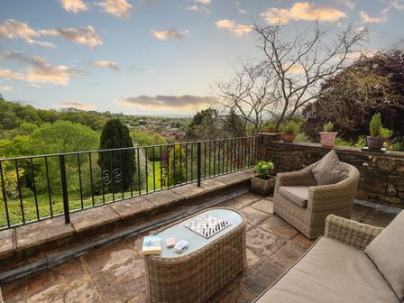 An outdoor patio with wicker furniture a chessboard playing cards and potted plants overlooking a green landscape at The Grooms in Lydney