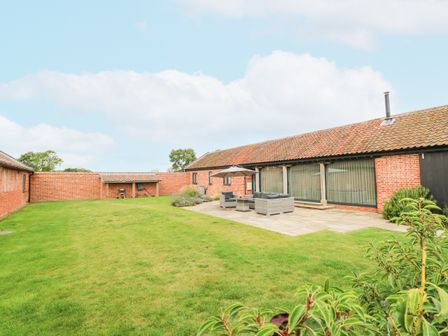 A garden with a tiled patio and outdoor seating in front of a red brick building at Shorthorn Barn in Attlebridge near Taverham