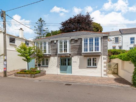 A two story house with bay windows and a green door next to a raised flower bed on a paved street at Armando in Devoran Cornwall