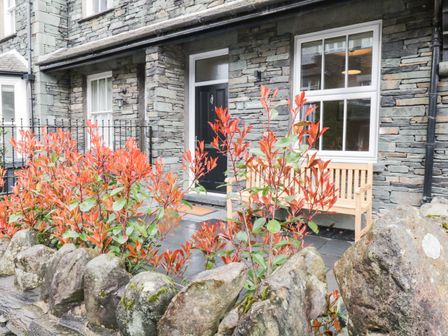 Front porch with a black door stone wall wooden bench red bushes and a stone fence at Netherbeck in Ambleside