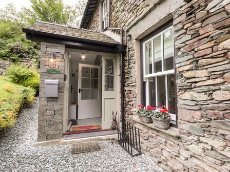 An open doorway to a stone house with flower pots on the window sill at Eller Close House in Grasmere
