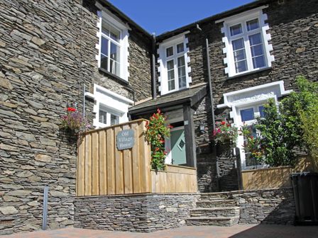 Stone exterior of a house with white window frames wooden fence and plants at Old Village House in Windermere