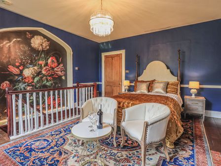 A bedroom with a bed two armchairs a small round table and a large floral mural on the wall at Wisteria in Grasmere