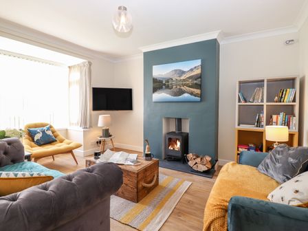 A living room with a wall-mounted tv a wood-burning stove a wooden coffee table and bookshelves at Pooley Howe in Keswick