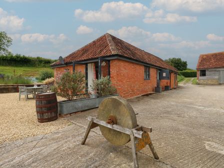 A brick building with a tiled roof and outdoor seating area near a sharpening stone and a wooden barrel at Swallows Nest in Puxey near Sturminster Newton