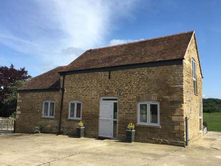A stone house with tiled roof four windows and a door with flowerpots outside at Shires Rest in Puxey near Sturminster Newton