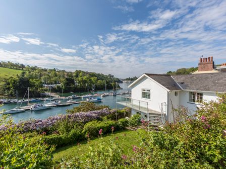 A white house with a balcony overlooking a river with boats and greenery at Creekside House in Fowey