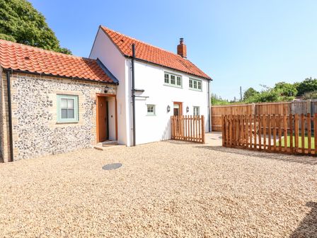 A cottage with tiled roof gravel driveway wooden fences and green lawn at Postbox Cottage in Feltwell