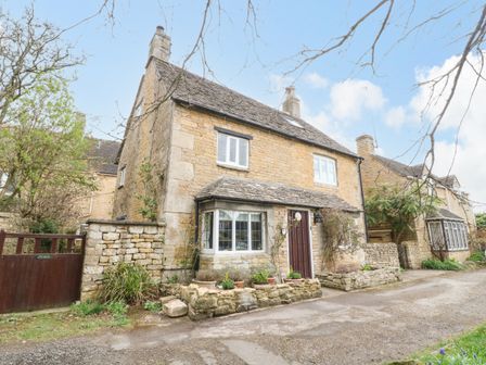 A stone cottage with two white windows a wooden door and stone planters at Tuesday Cottage in Bourton-On-The-Water