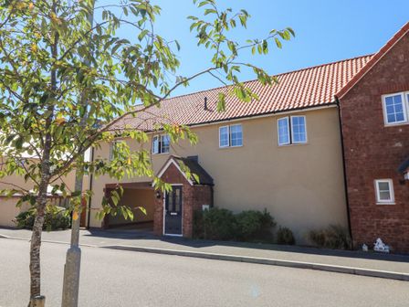 A residential building with a beige wall and red tiled roof next to a tree on a street at 1 Marsh Gardens in Dunster