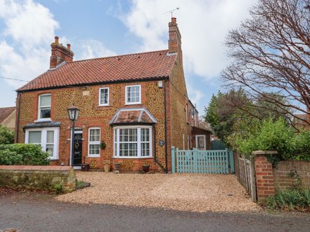 A stone and brick house with a gravel driveway and a blue wooden gate at Job's Cottage in Snettisham