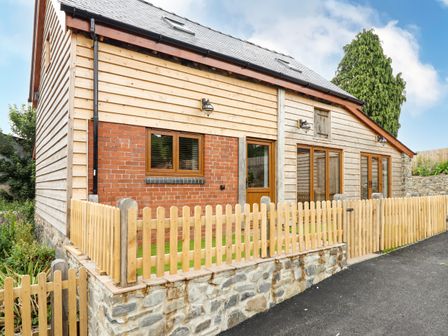 A wooden and brick house with a stone base and a wooden picket fence at Swallows Rest in Llandyssil near Montgomery