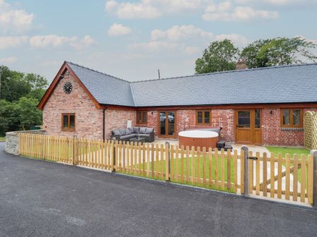 A brick house with a grey slate roof fenced garden outdoor sofa and hot tub at The Clockhouse in Llandyssil near Montgomery