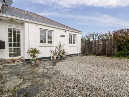 The exterior of a white house with a stone and gravel driveway and potted plants near the entrance at Badgers Way in Tintagel