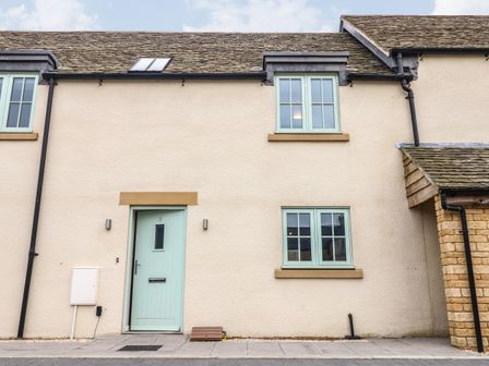 Front view of a cream colored house with a pale green door and windows at 9 Windrush Heights in Burford