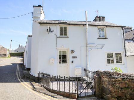 A white house with a small fenced front yard and a satellite dish on a corner by the street at Bryn Coed in Porthmadog