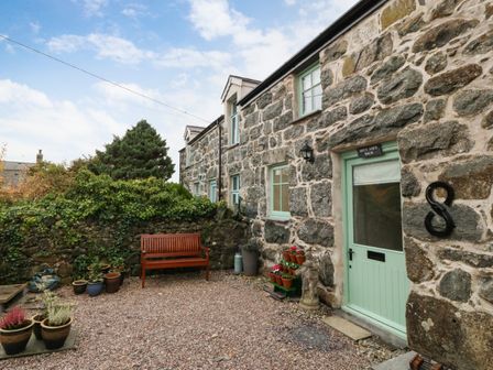 A stone cottage exterior with a green door and windows a wooden bench and potted plants at Bryn Aber Bach in Llangybi Gwynedd