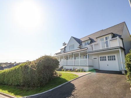 A white two-story house with a pitched roof driveway and trimmed bushes at Haul A Gwynt in Criccieth
