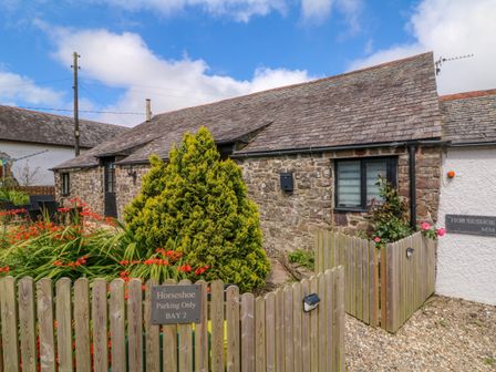 A stone cottage with a wooden fence and garden with flowers at Horseshoe Cottage in Hartland