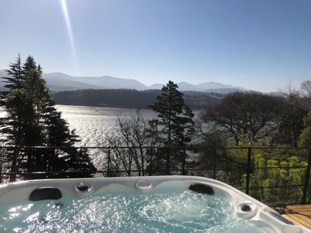 An outdoor hot tub with bubbling water overlooking a lake trees and mountains at Afallon in Menai Bridge