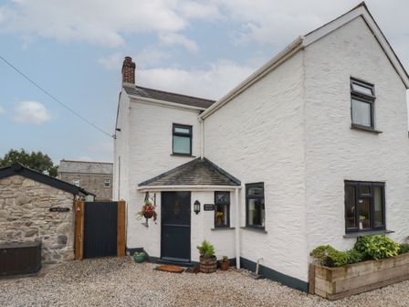 A white two story house with black windows and door surrounded by gravel and plants at Miners cottage in St Austell