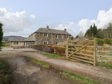 A stone house with a gravel driveway and a wooden gate at Glen Cottage in Troutbeck near Keswick
