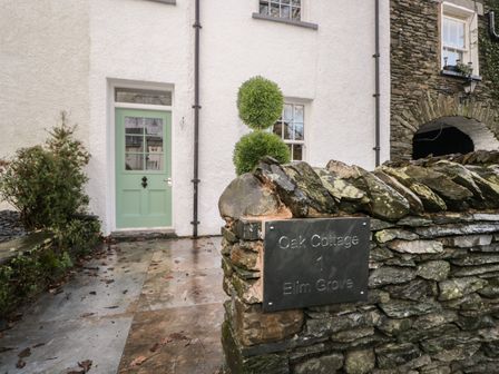 A stone wall with a sign reading Oak Cottage 1 Elim Grove in front of a house with a green door at Oak Cottage in Windermere