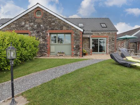 A stone cottage with a gravel path leading to the door and lounge chairs on the lawn at Barcud Cottage in Golden Grove near Llandeilo