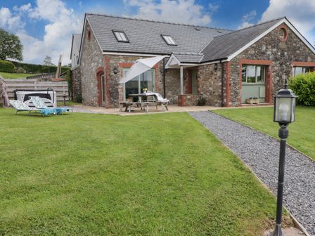 Stone cottage with slate roof and green lawn with sun loungers and a picnic table under an umbrella at Gwennol Cottage Golden Grove near Llandeilo